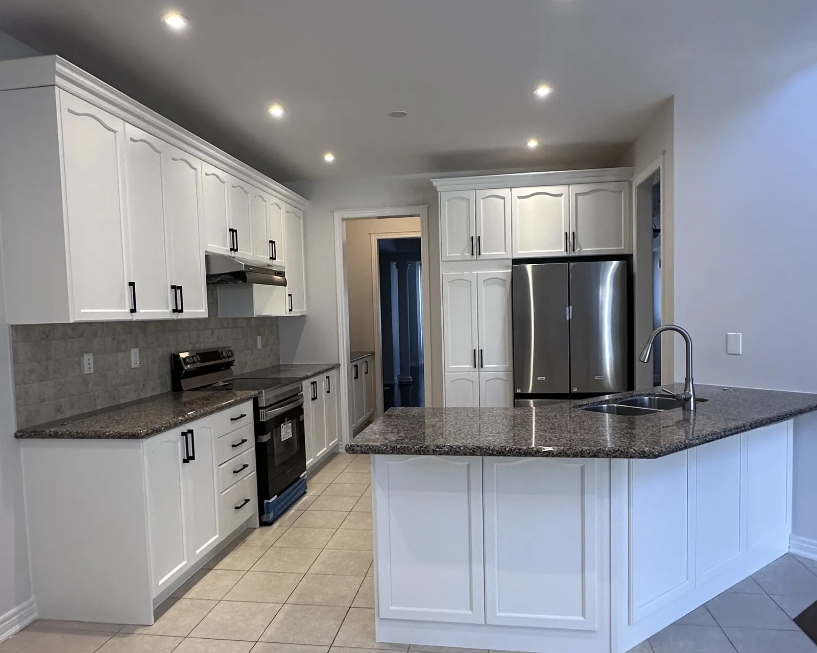 After — A kitchen before and after refacing — cherry raised-panel fronts replaced with white, on the same cabinet boxes, with the original granite and tile floor kept