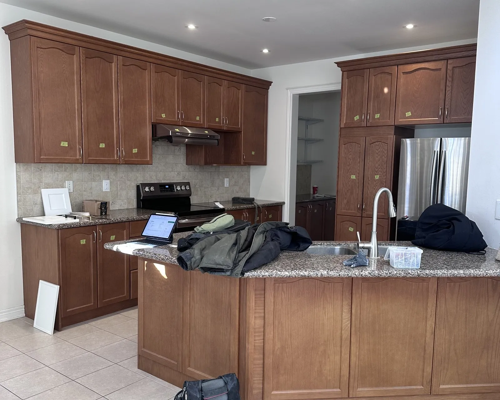 Before — A kitchen before and after refacing — cherry raised-panel fronts replaced with white, on the same cabinet boxes, with the original granite and tile floor kept