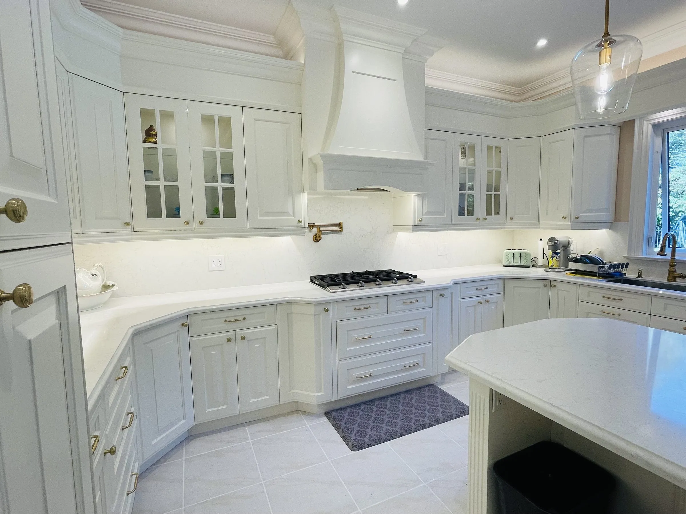 A kitchen in Gormley refaced by Kitchen Made New, with white raised-panel doors, a custom range hood and quartz countertops that run to the island