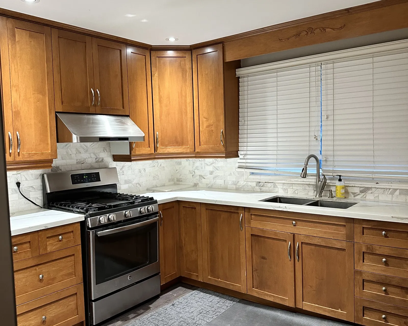 Before — A kitchen before and after — oak fronts replaced with white and new veined stone run across the counters, the range wall and window unchanged