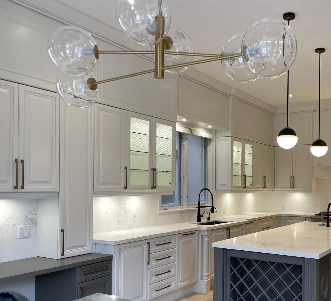 After — A kitchen before and after. Cream raised-panel cabinets with a glazed finish became white, and the island was refinished in charcoal and kept its wine rack