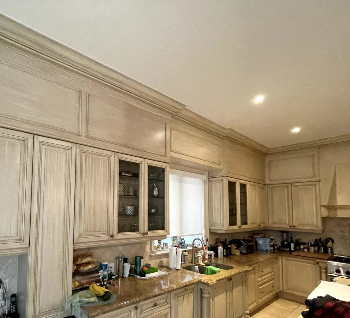 Before — A kitchen before and after. Cream raised-panel cabinets with a glazed finish became white, and the island was refinished in charcoal and kept its wine rack