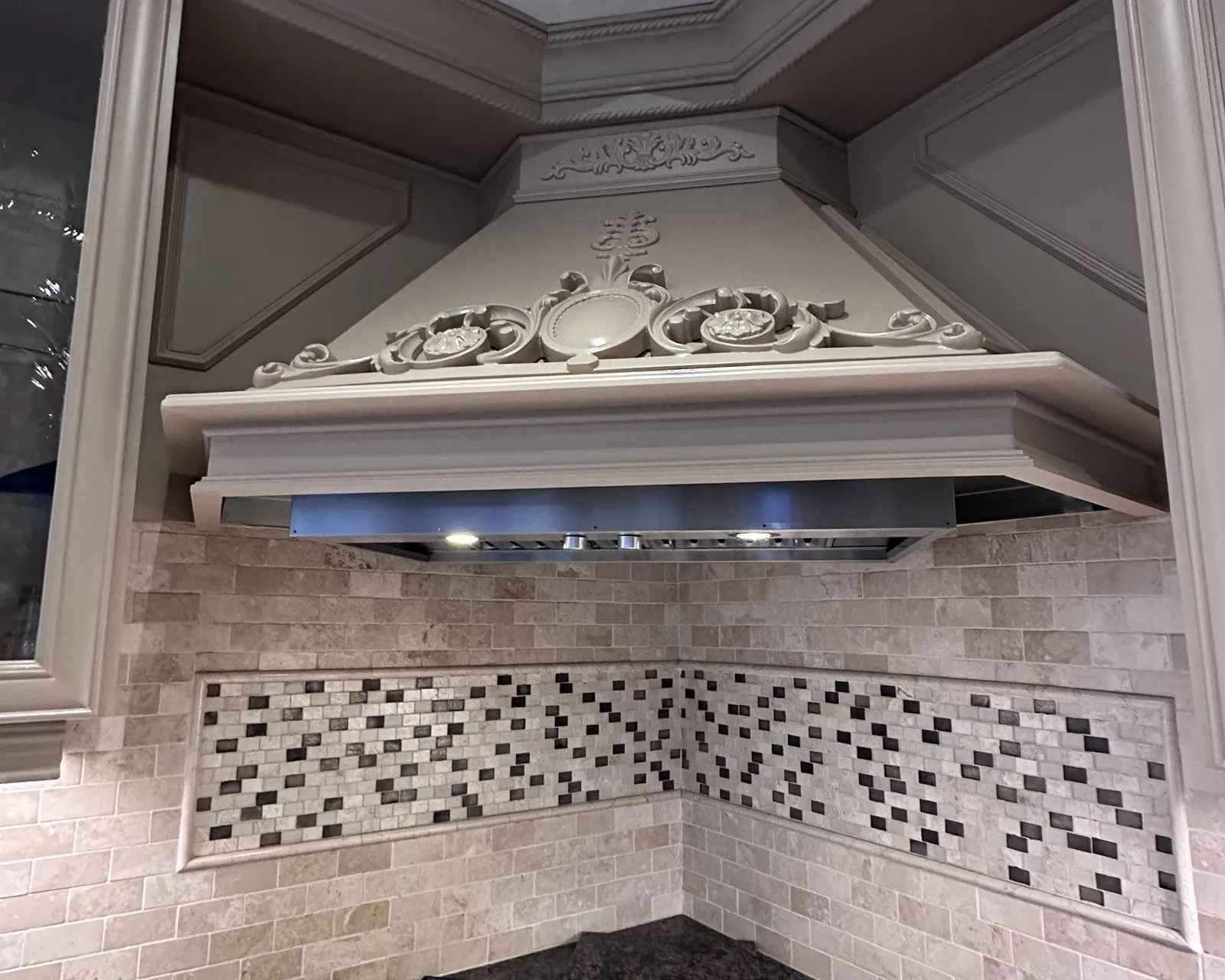 A carved range-hood surround finished to match the cabinetry, the moulding and scrollwork covered without the detail filling in