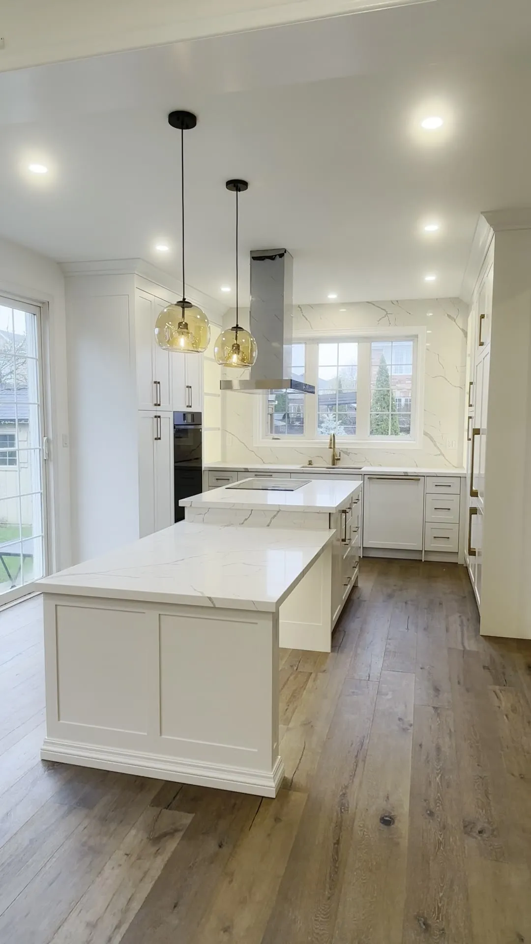 A finished custom kitchen in Toronto with white shaker cabinets, a waterfall marble-look island and a stainless hood, shown room by room