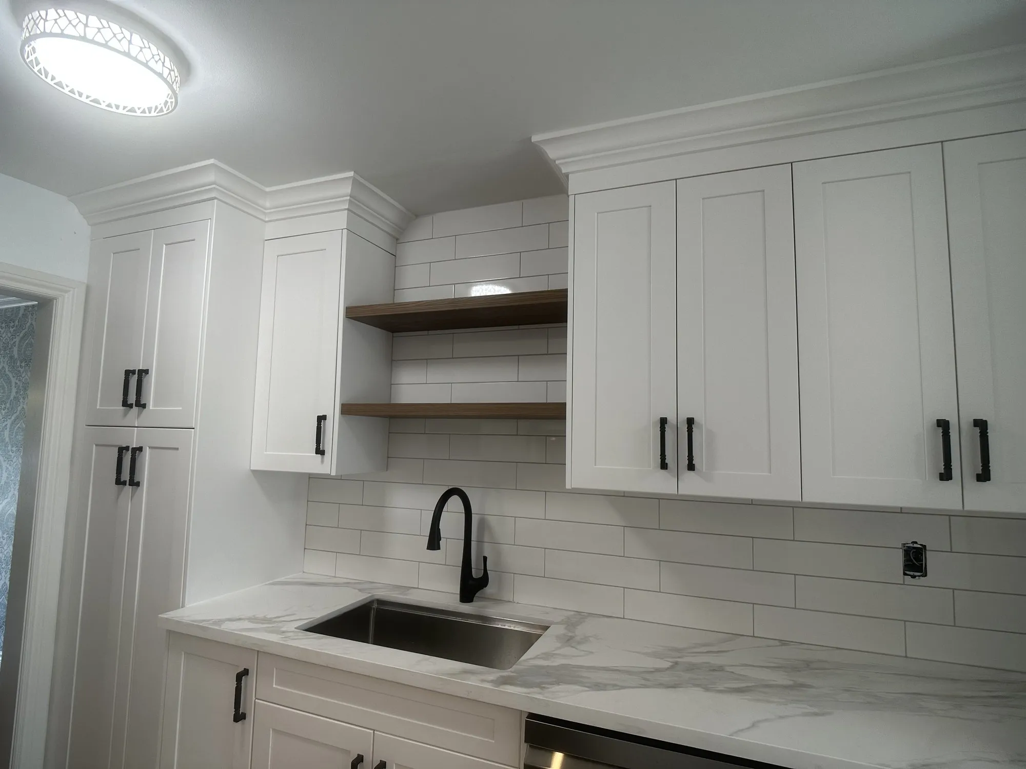 The finished sink run with two floating wood shelves above it, quartz counter, subway tile and a black tap