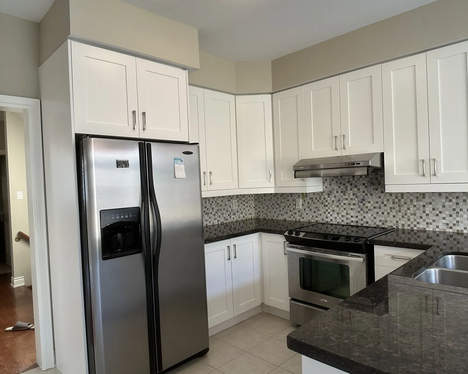 A kitchen before and after. Dark cherry doors were replaced with white on the same boxes, and the granite, mosaic backsplash and tile floor all stayed