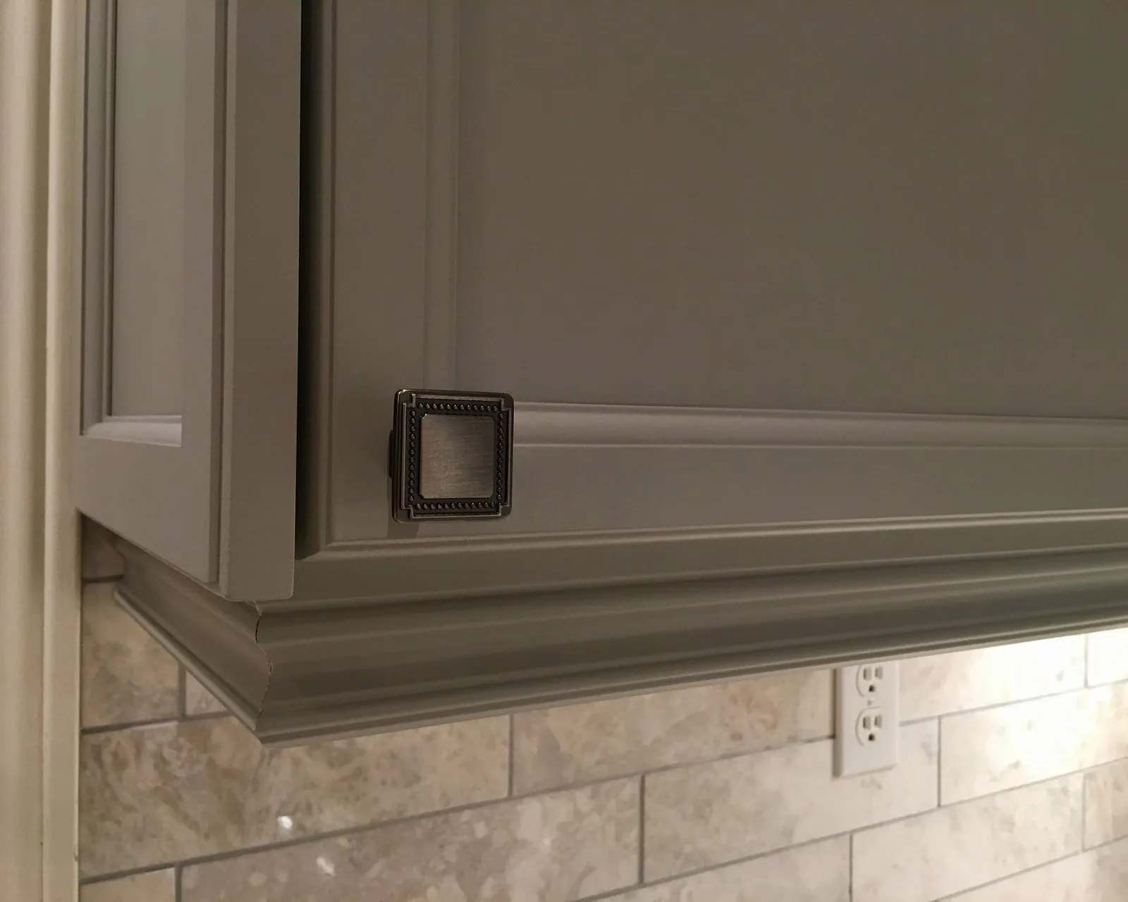 A sprayed cabinet door and crown moulding in matte grey, the corner and hardware visible with no brush marks or texture