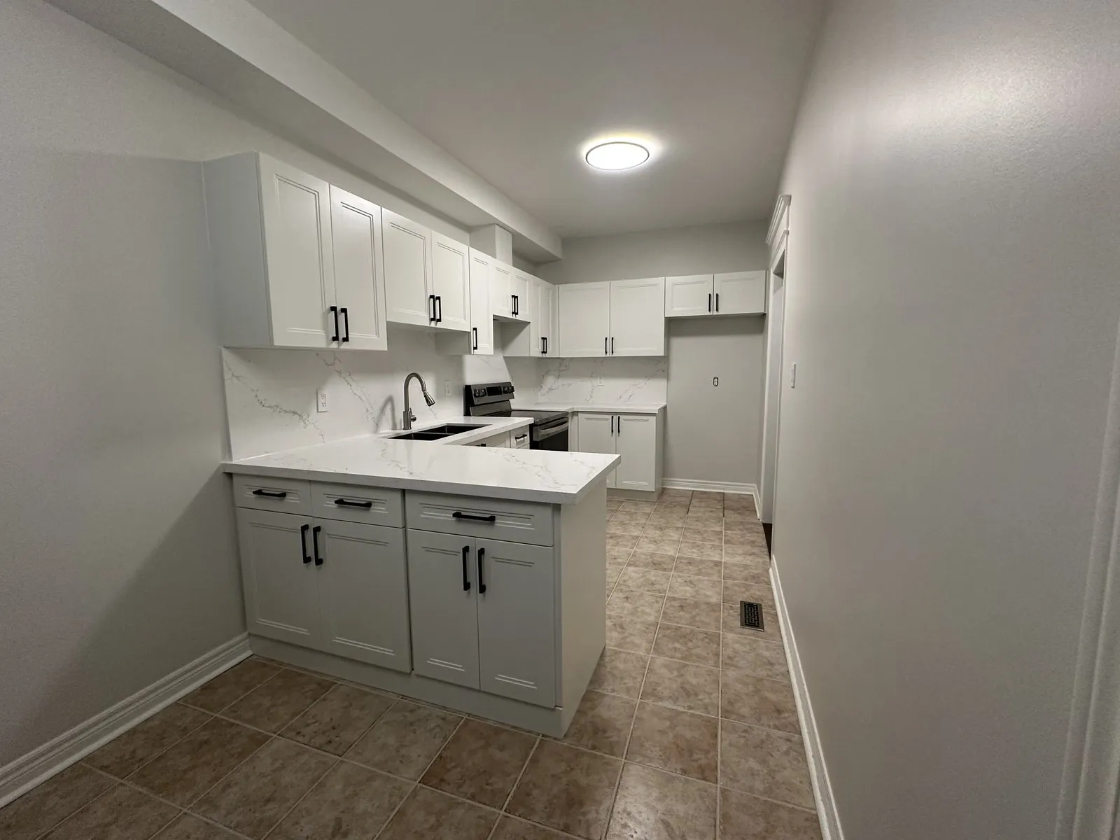 A refaced kitchen with new white shaker doors, drawer fronts and black bar handles on the original cabinet boxes, under a veined quartz counter
