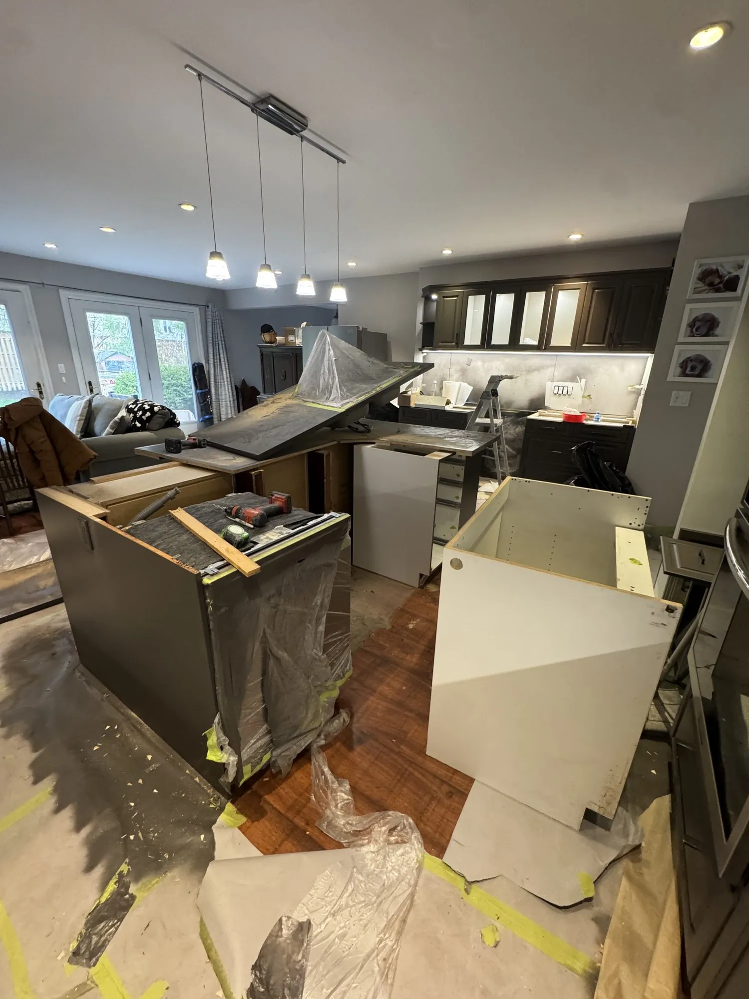 The sink run stripped out, the old countertop lifted off and two new white cabinet boxes standing ready, with the floor papered and taped