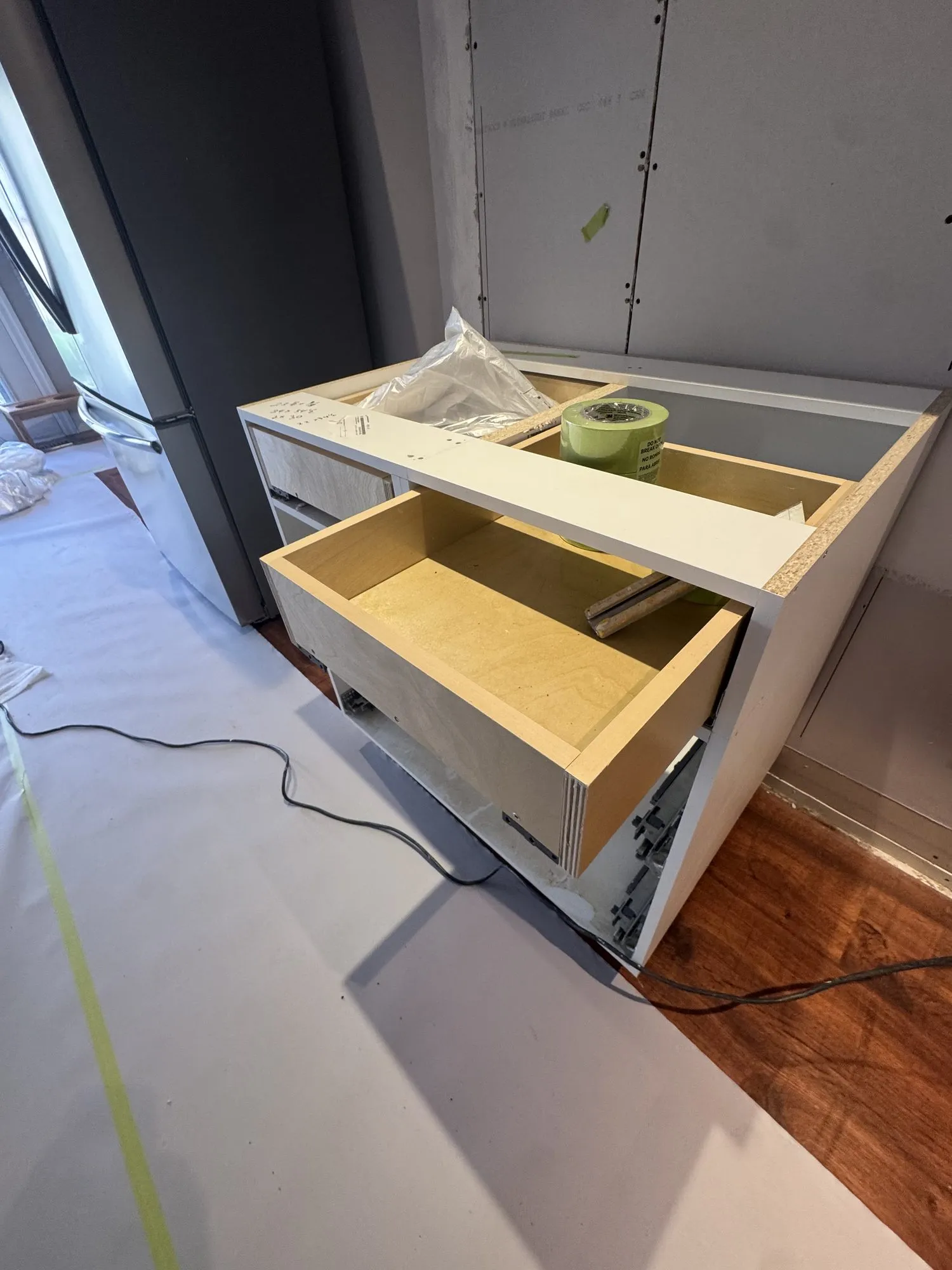 A plywood drawer box pulled open in one of the new cabinets, the natural ply visible against the white box