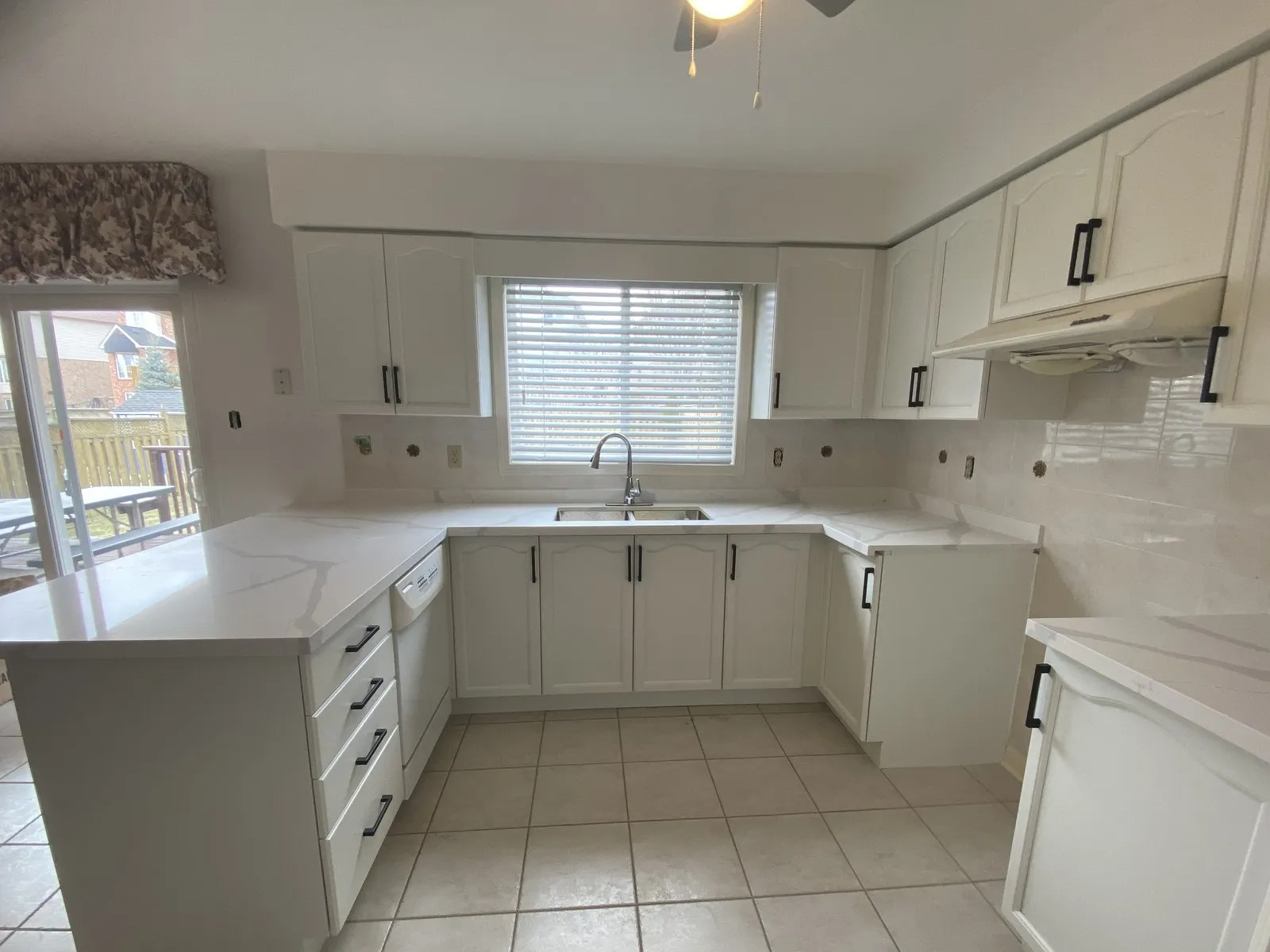 A whole U-shaped kitchen in one frame — eight upper doors, six lower doors and four drawer fronts sprayed white with black bar pulls, the backsplash stripped and waiting on the tiler