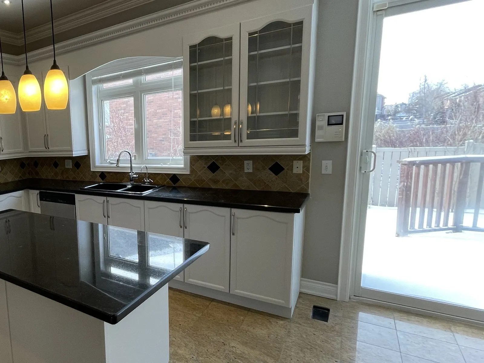 A family kitchen with its doors sprayed white and the black granite kept — glass-front uppers over the sink, an island in the foreground, and the patio door opening onto a snow-covered deck